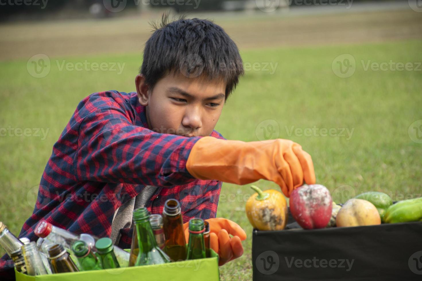 Young asian boy sorting various garbages and putting them into the boxes infront of him in the park, nature care and environment love concept. photo