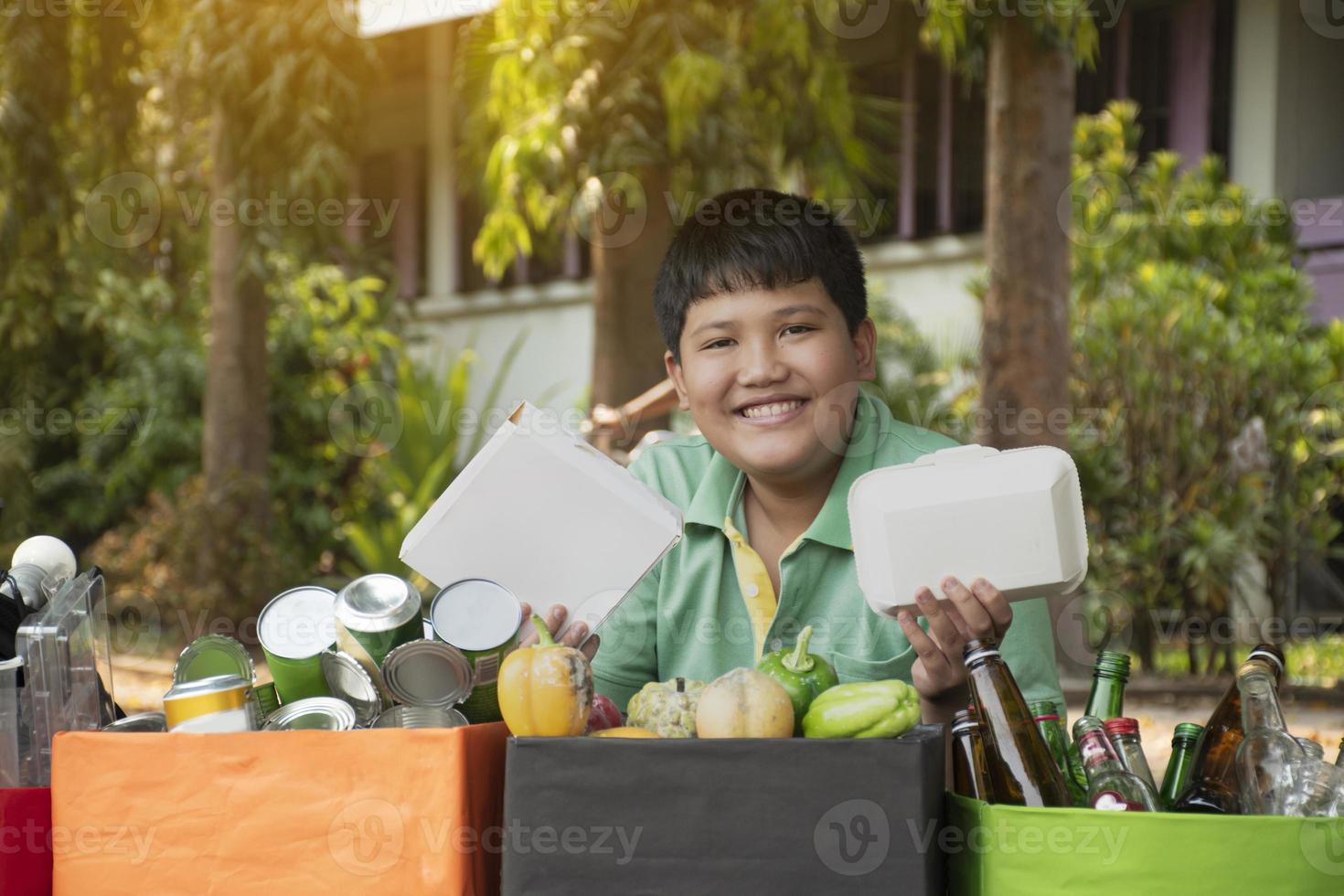 Asian boy is separating garbages and putting them into the boxes in front of him near building, soft and selective focus, environment care, community service and summer vacation activities concept. photo