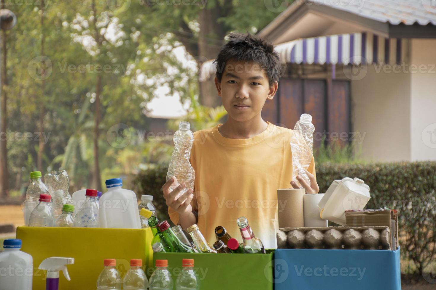 Young asian boy sorting various garbages and putting them into the boxes infront of him in the park, nature care and environment love concept. photo