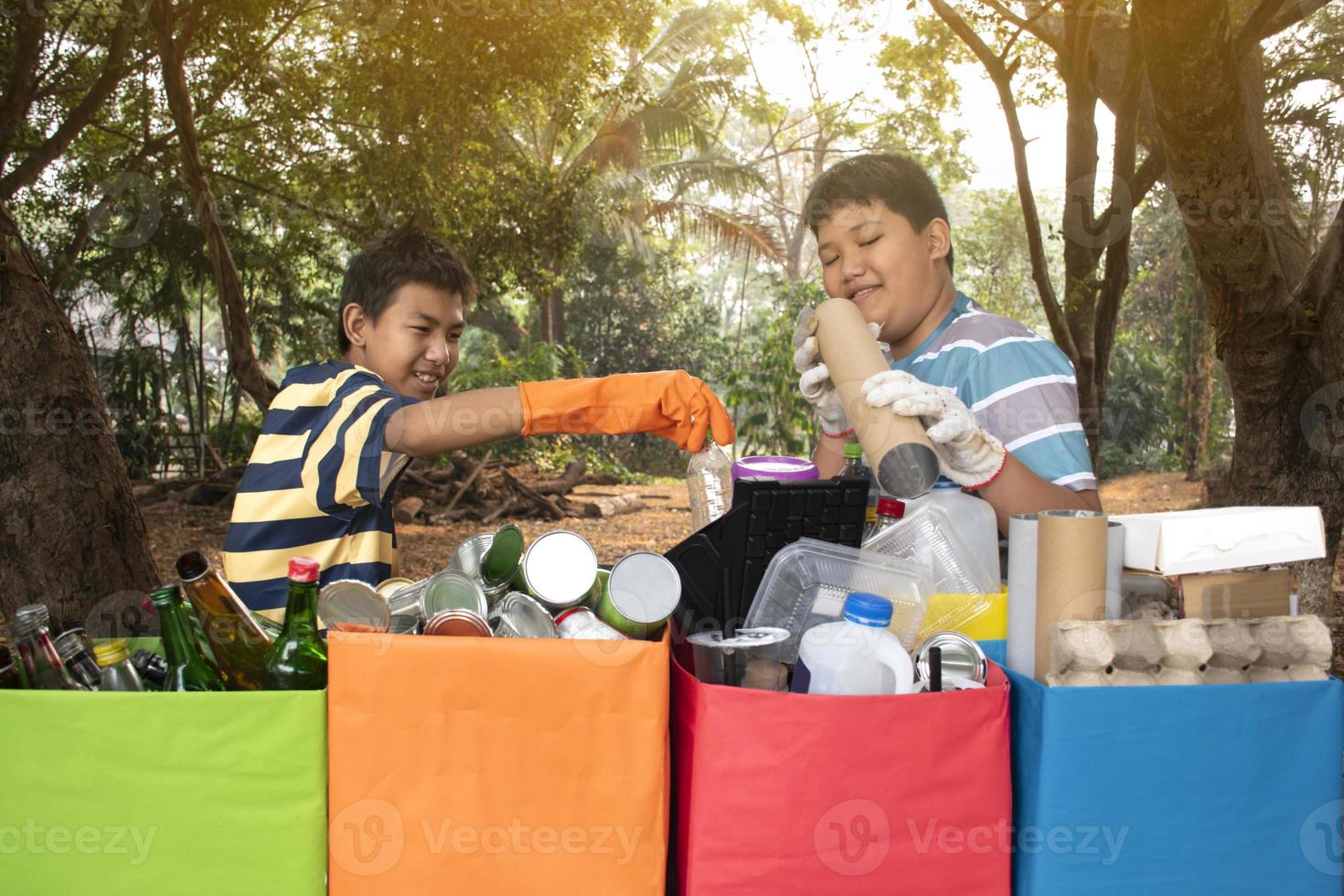 Young asian boy sorting various garbages and putting them into the boxes infront of him in the park, nature care and environment love concept. photo