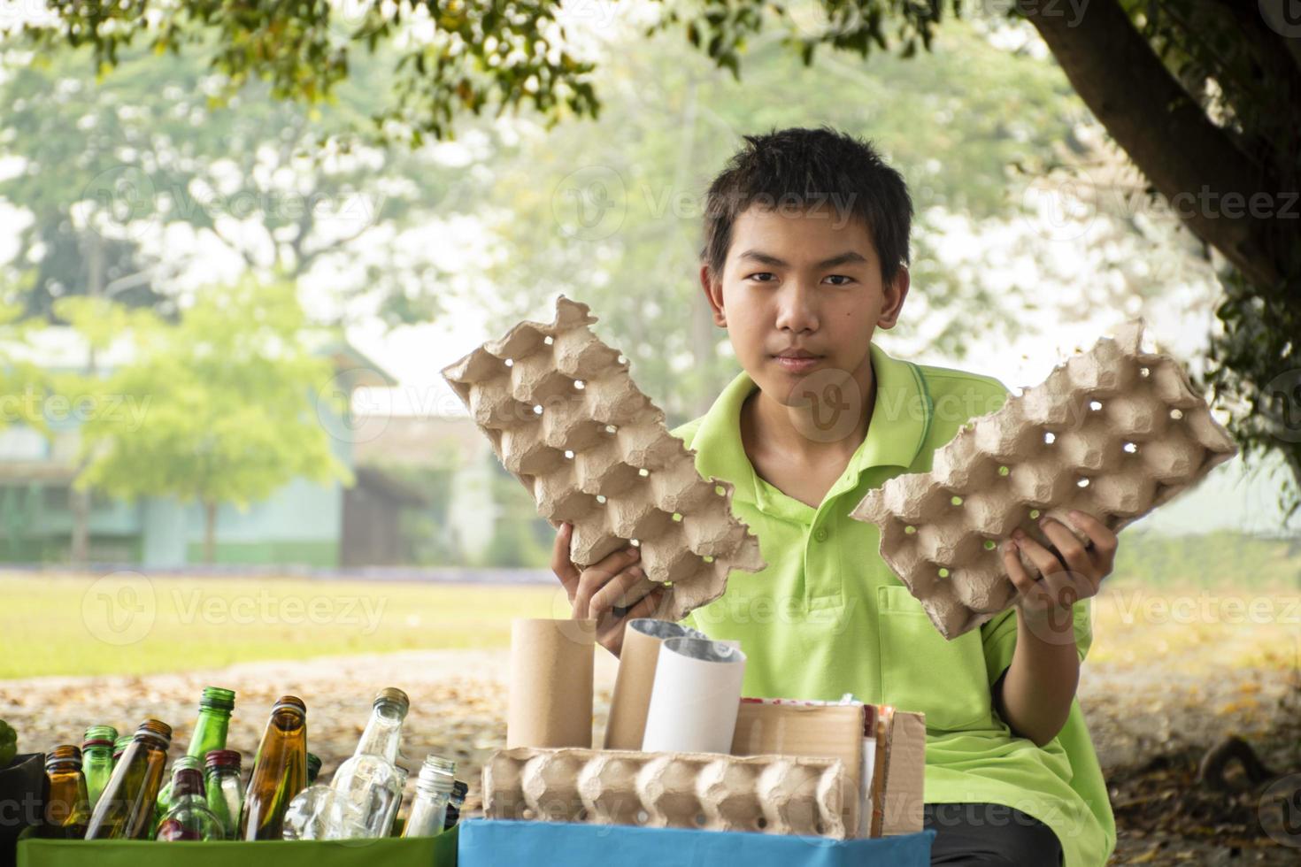 Young asian boy sorting various garbages and putting them into the boxes infront of him in the park, nature care and environment love concept. photo