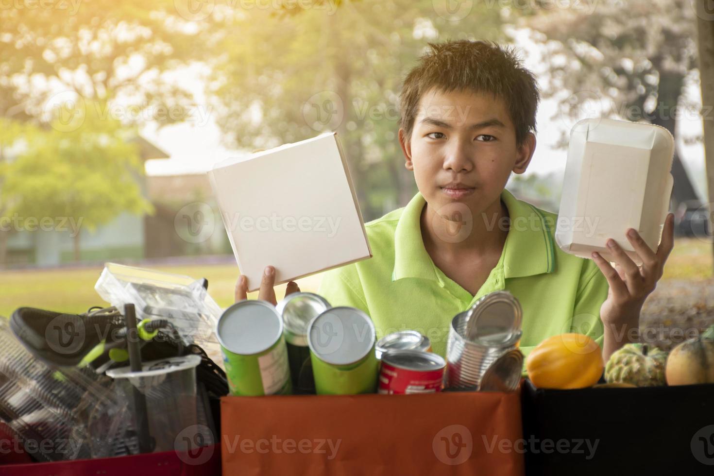 Young asian boy sorting various garbages and putting them into the boxes infront of him in the park, nature care and environment love concept. photo