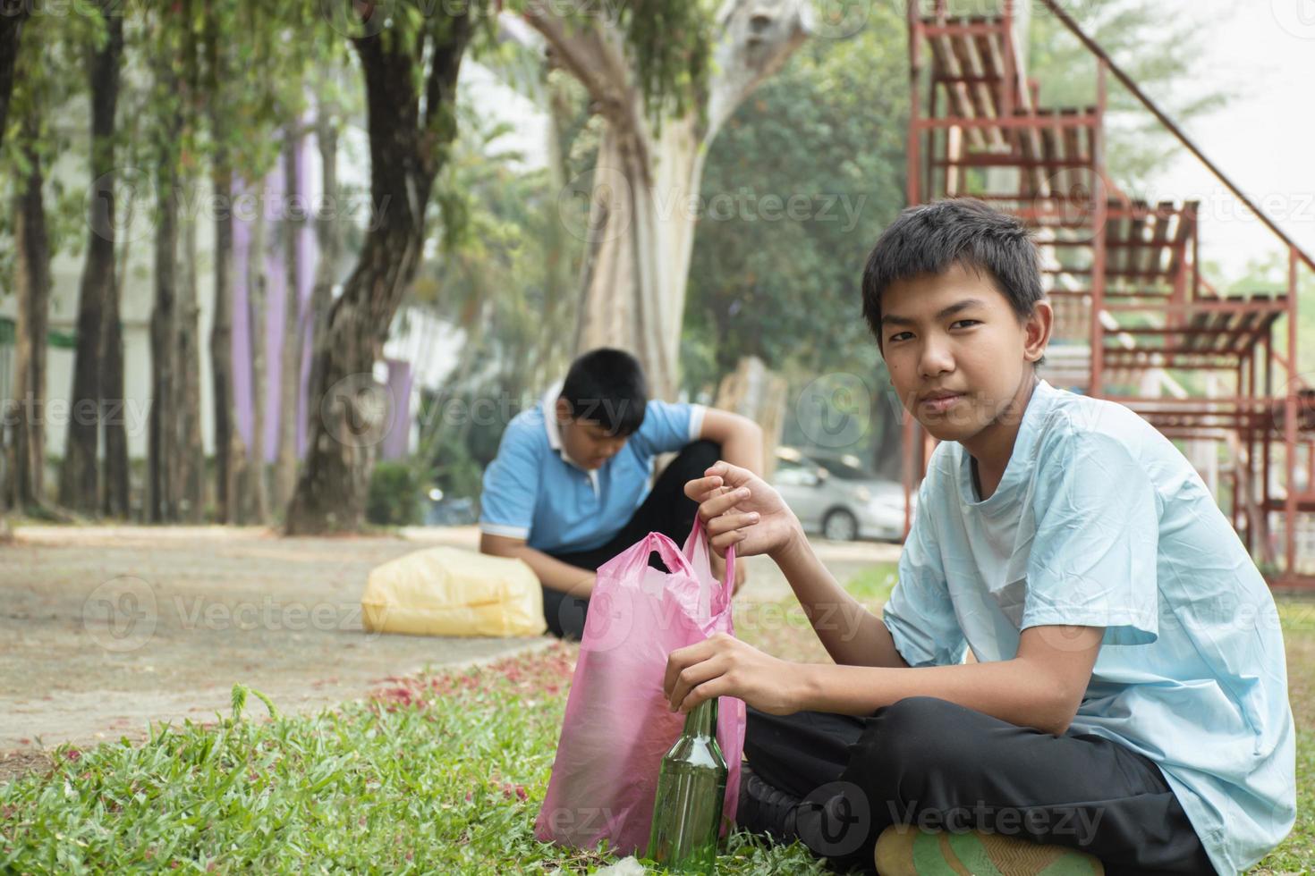 Young asian boy sorting various garbages and putting them into the boxes infront of him in the park, nature care and environment love concept. photo