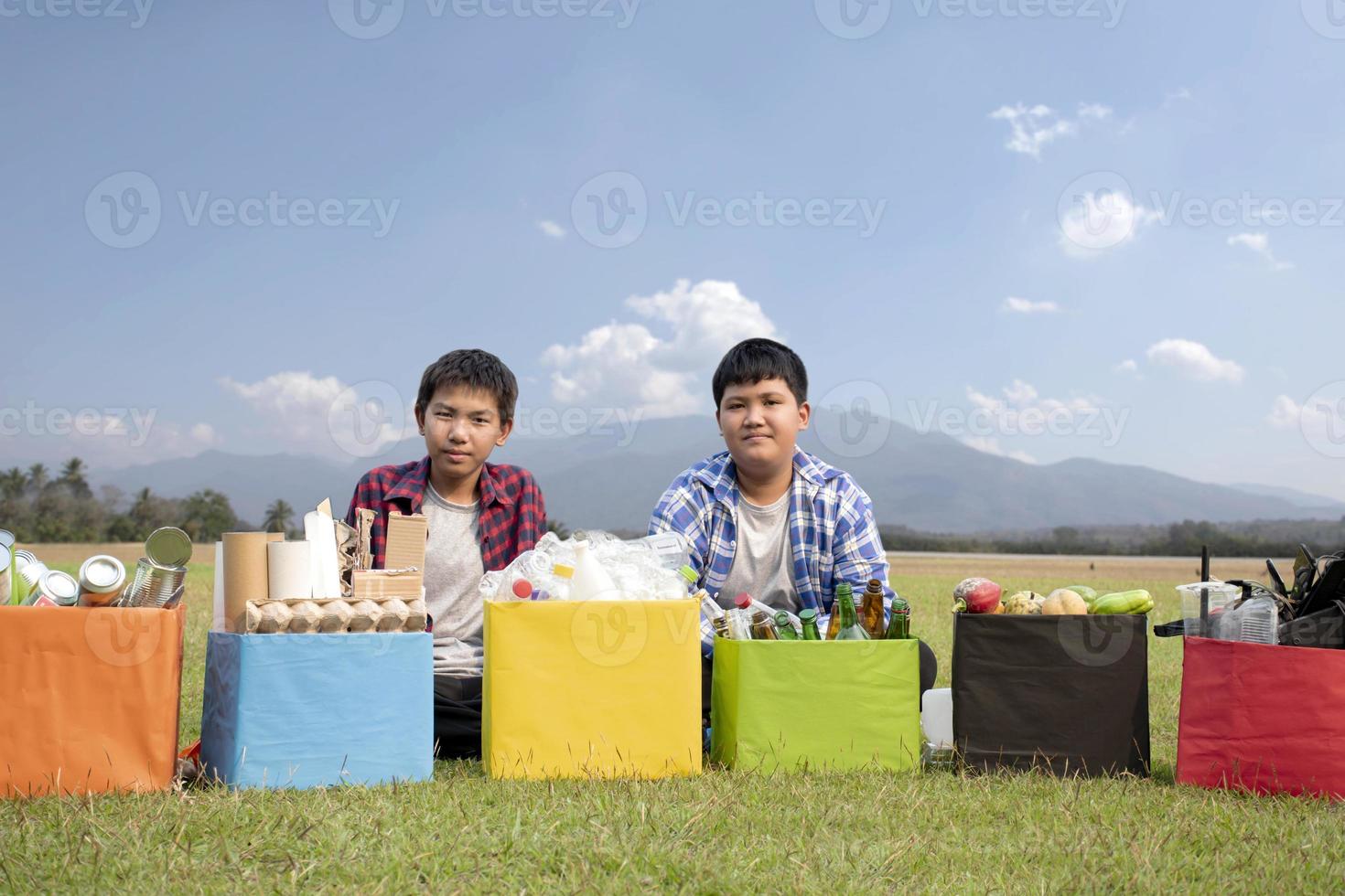 Young asian boy sorting various garbages and putting them into the boxes infront of him in the park, nature care and environment love concept. photo