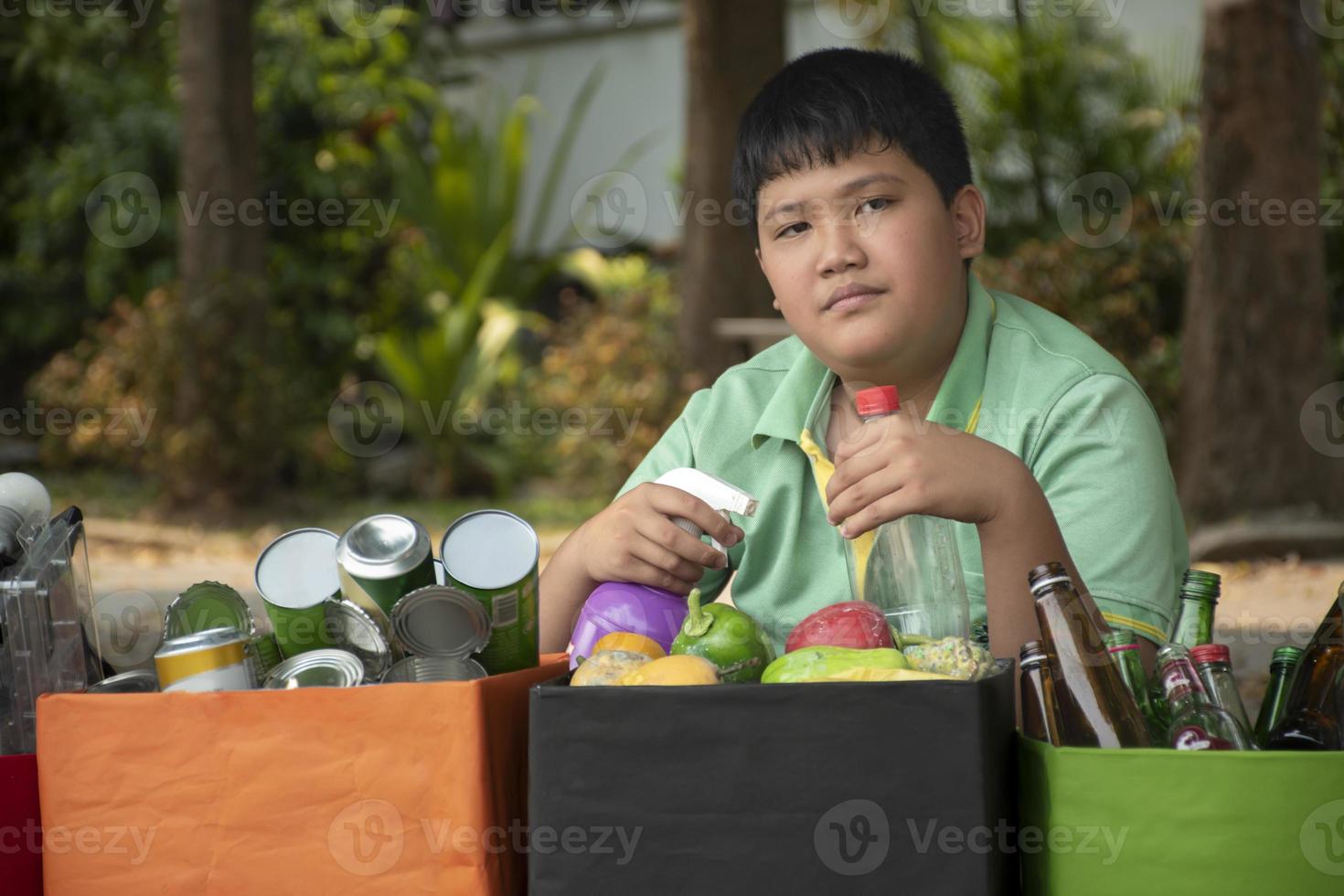 Asian boy is separating garbages and putting them into the boxes in front of him near building, soft and selective focus, environment care, community service and summer vacation activities concept. photo