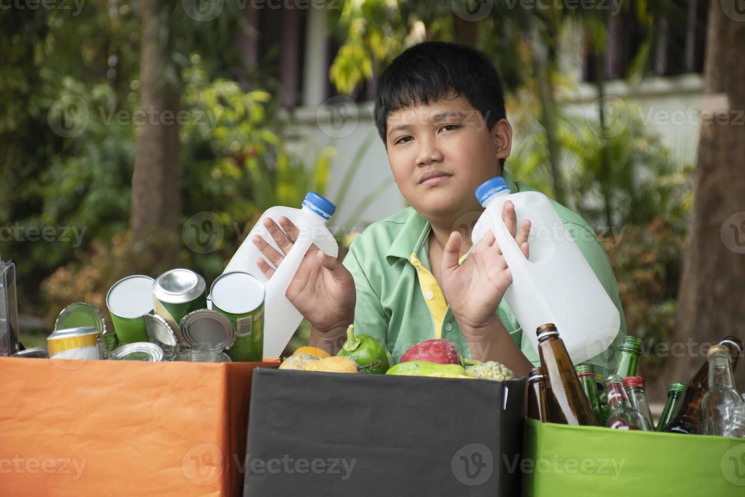 Asian boy is separating garbages and putting them into the boxes in front of him near building, soft and selective focus, environment care, community service and summer vacation activities concept. photo