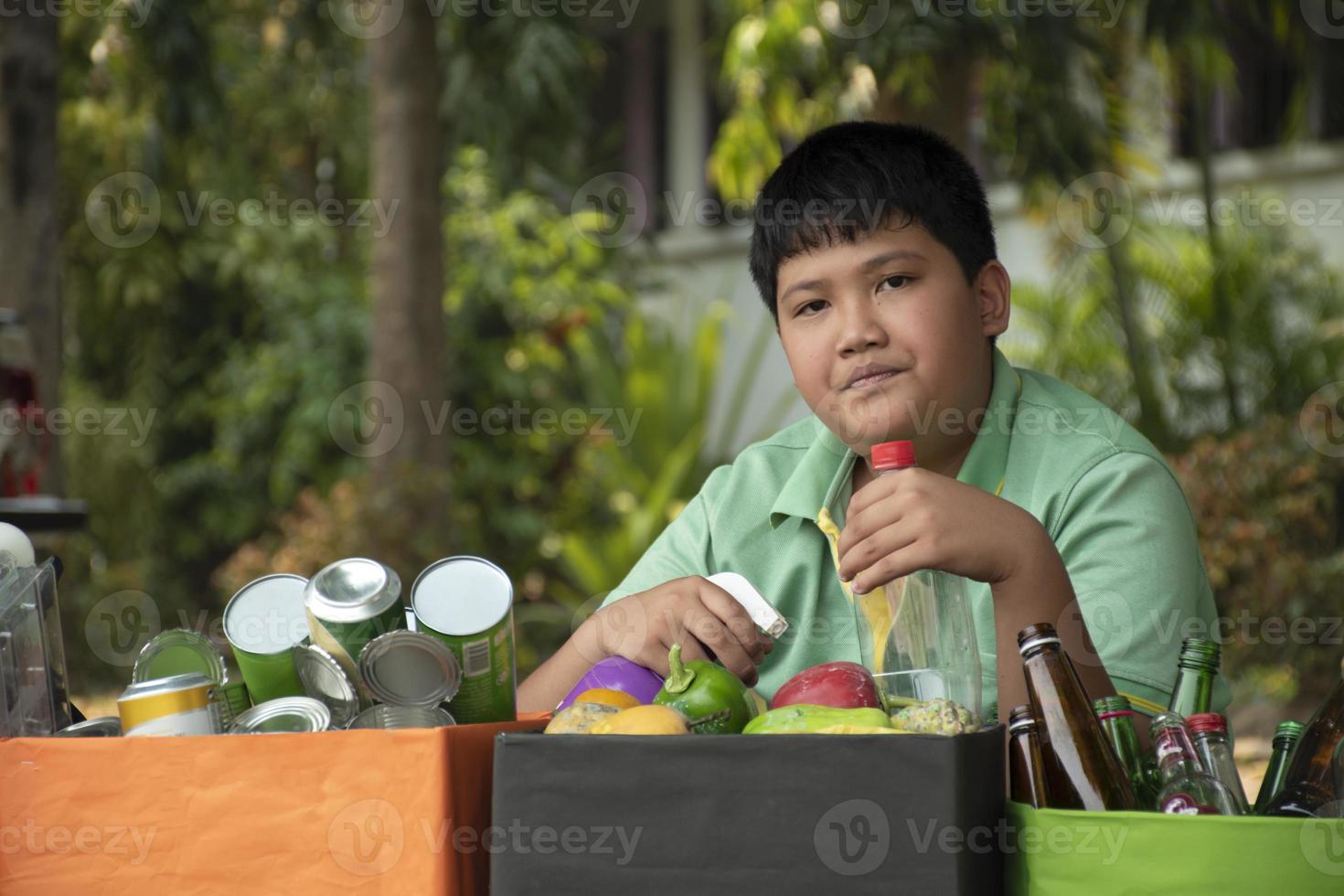 Asian boy is separating garbages and putting them into the boxes in front of him near building, soft and selective focus, environment care, community service and summer vacation activities concept. photo