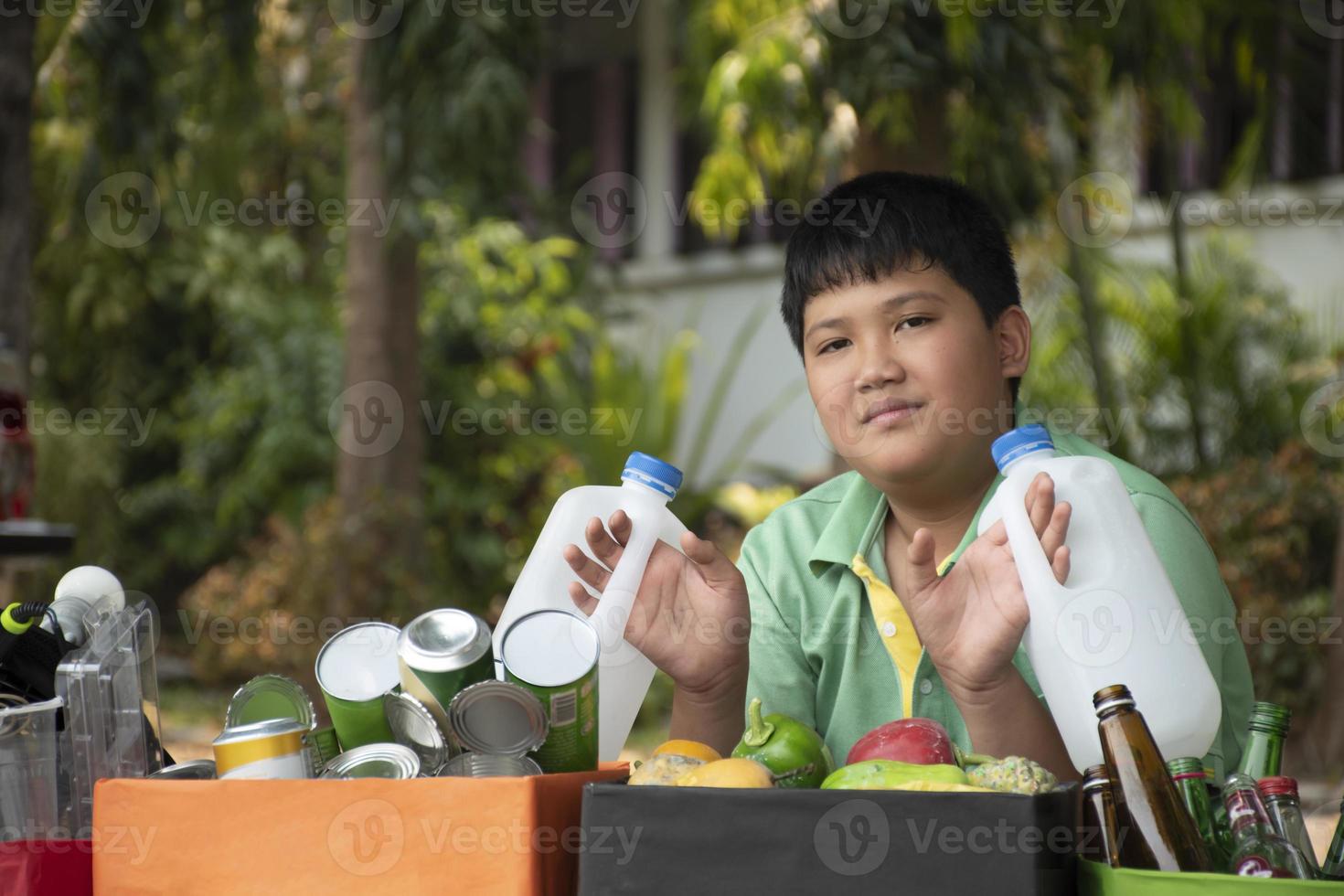 Asian boy is separating garbages and putting them into the boxes in front of him near building, soft and selective focus, environment care, community service and summer vacation activities concept. photo