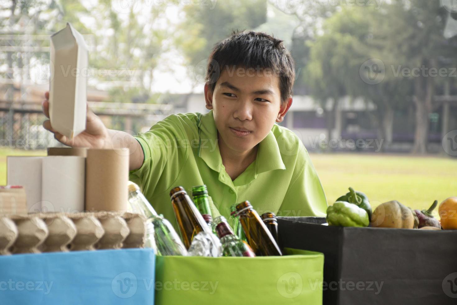 Young asian boy sorting various garbages and putting them into the boxes infront of him in the park, nature care and environment love concept. photo