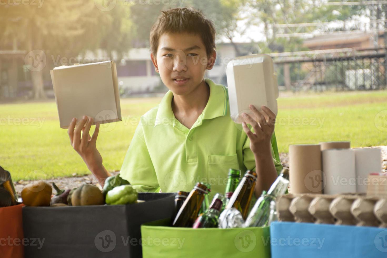 Young asian boy sorting various garbages and putting them into the boxes infront of him in the park, nature care and environment love concept. photo
