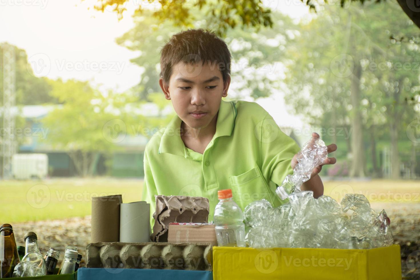 Young asian boy sorting various garbages and putting them into the boxes infront of him in the park, nature care and environment love concept. photo