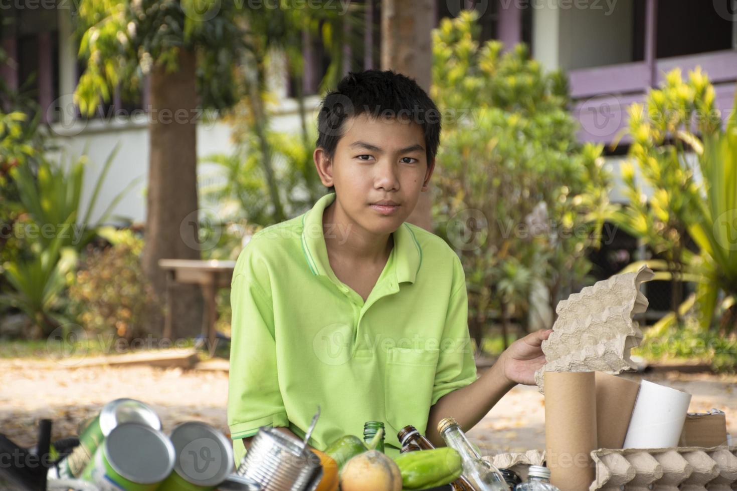 Young asian boy sorting various garbages and putting them into the boxes infront of him in the park, nature care and environment love concept. photo