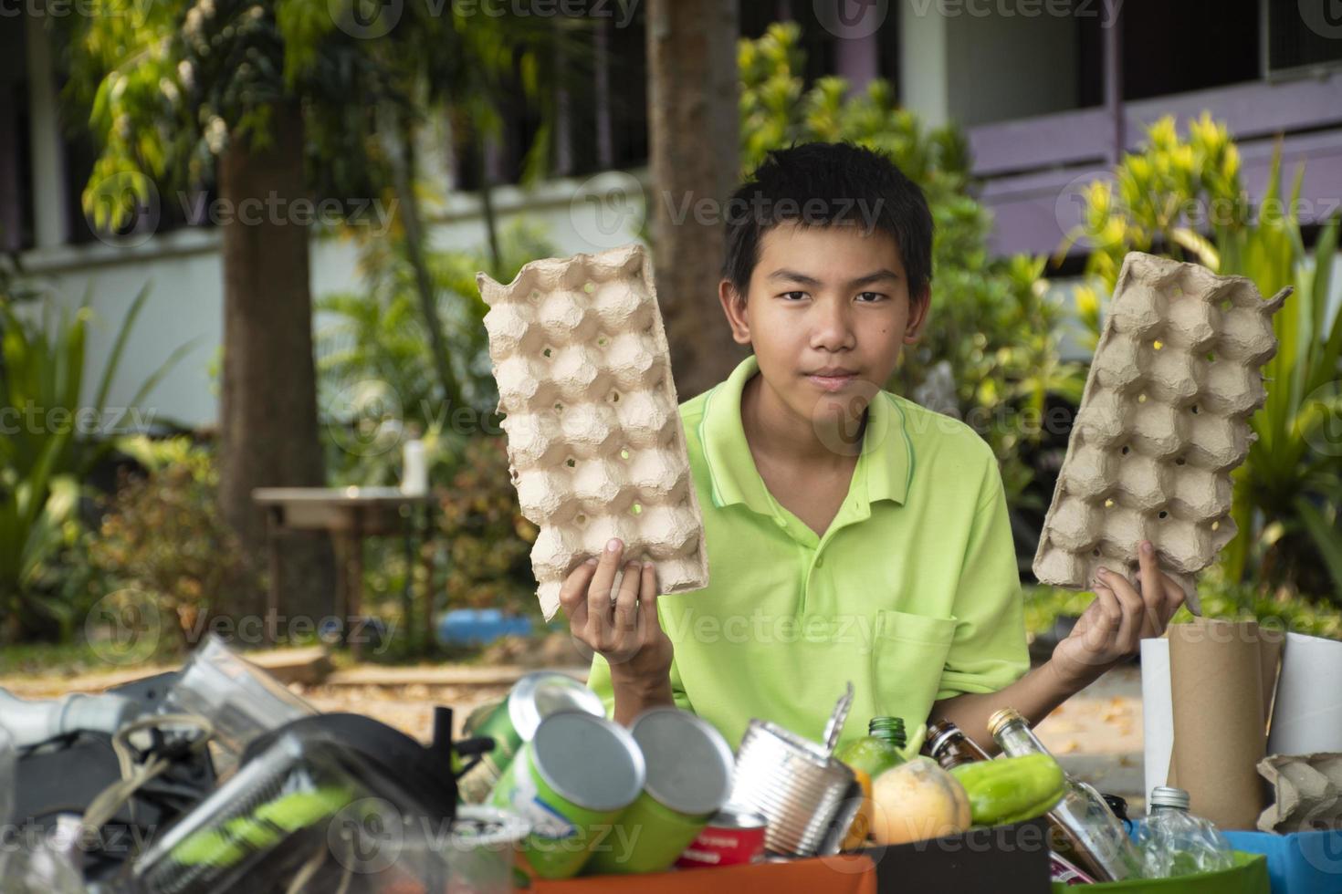 Young asian boy sorting various garbages and putting them into the boxes infront of him in the park, nature care and environment love concept. photo
