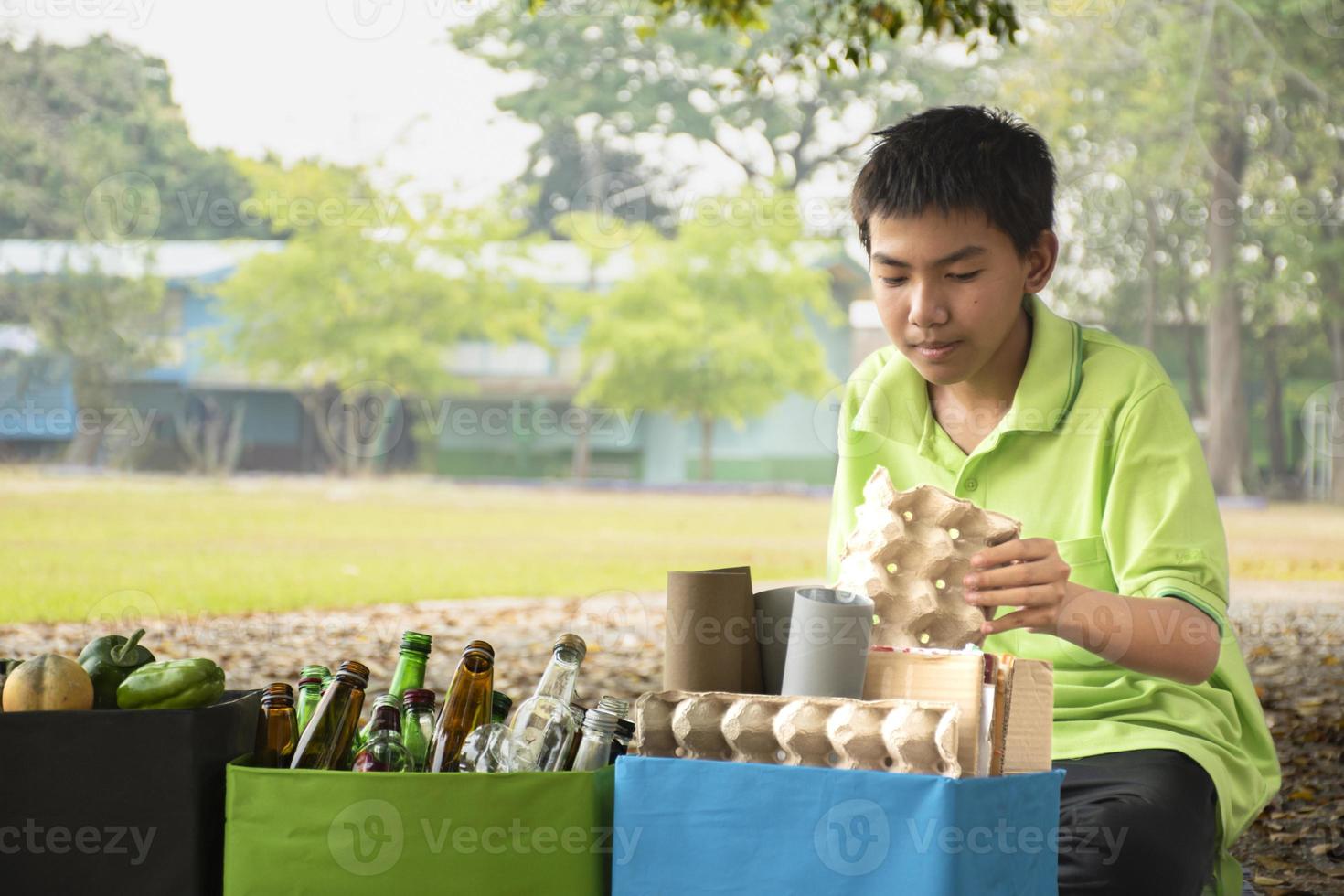 Young asian boy sorting various garbages and putting them into the boxes infront of him in the park, nature care and environment love concept. photo