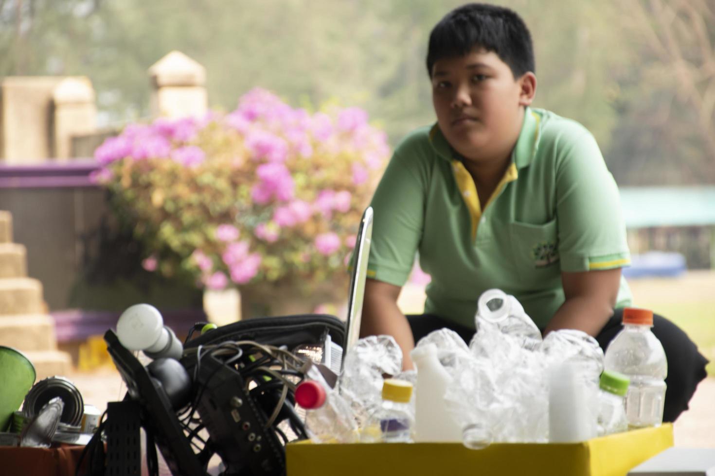Asian boy in green t-shirt is separating different types of trash into color-coded boxes in the back of a pickup truck before leading them to sell and generate income after their school holidays. photo