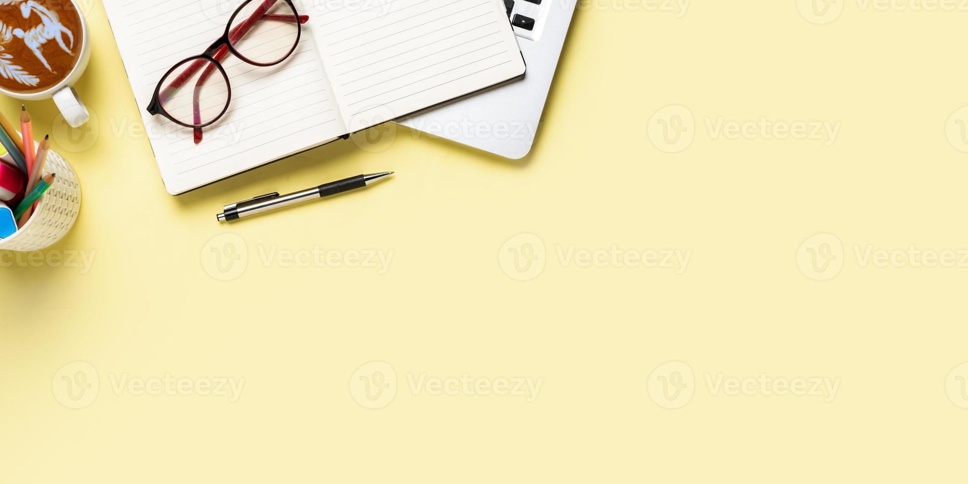 Office desk with computer, Notebook, pen, Cup of coffee on yellow background, Top view with copy space, Mock up. photo