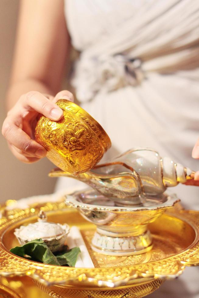 mujer mano hoding oro taza para verter agua en concha cáscara en glod bandeja en tradicion tailandés Boda ceremonia foto