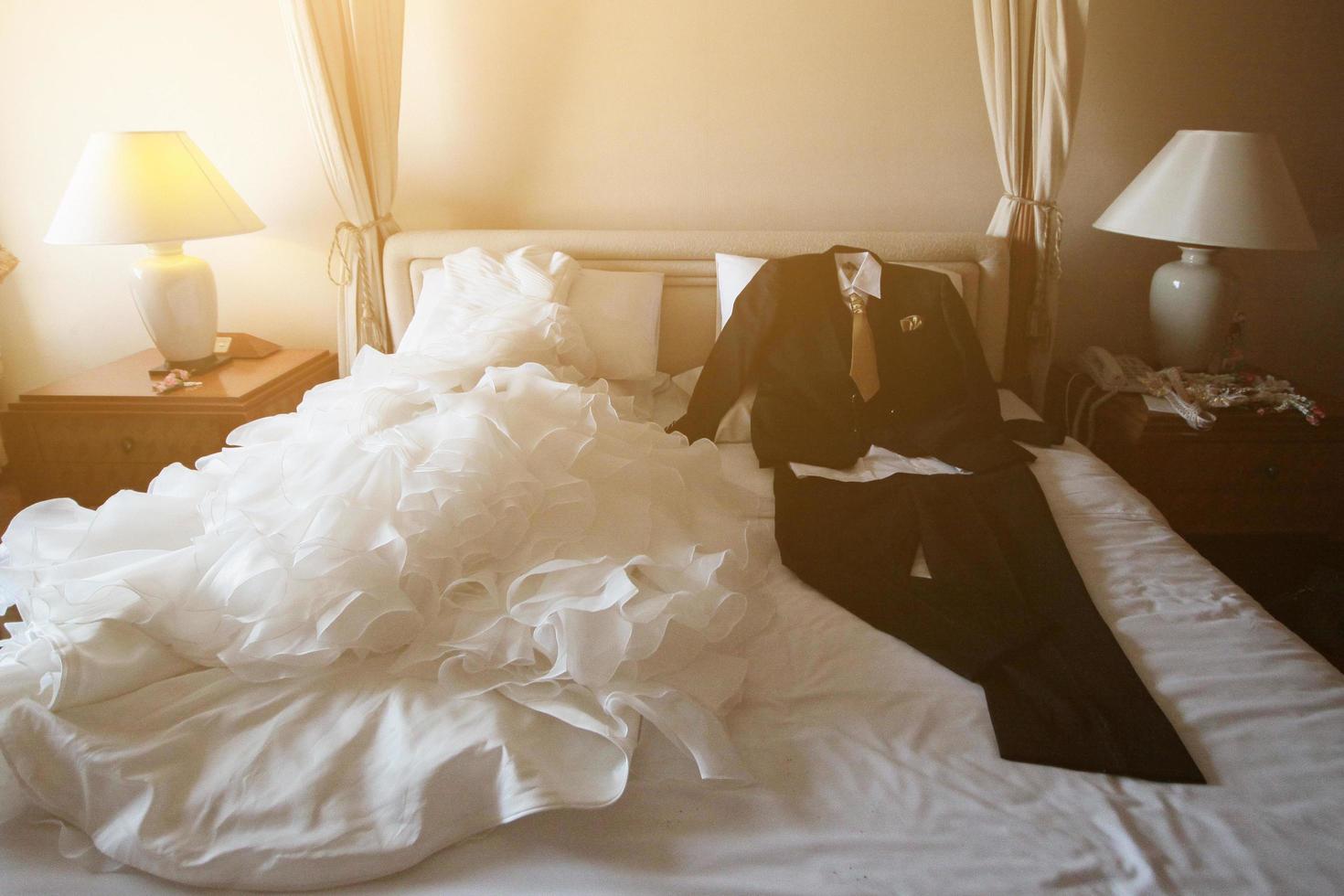 Boda vestir y traje acostado en el blanco cama con hermosa Dom ligero en hotel habitación. san valentin día y amor para celebracion concepto. foto