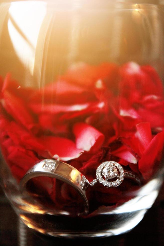 Silver and Diamond rings of Groom and bride in Wide glass with red Rose petals. Valentines day and love for celebration concept. photo