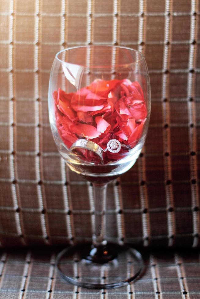 Silver and Diamond rings of Groom and bride in Wide glass with red Rose petals. Valentines day and love for celebration concept. photo