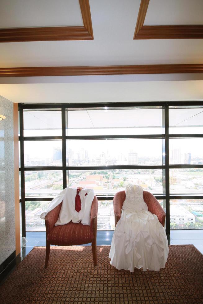 Wedding Dress and suit lying on armchair in wedding ceremony. Groom and Bride clothes concept. photo