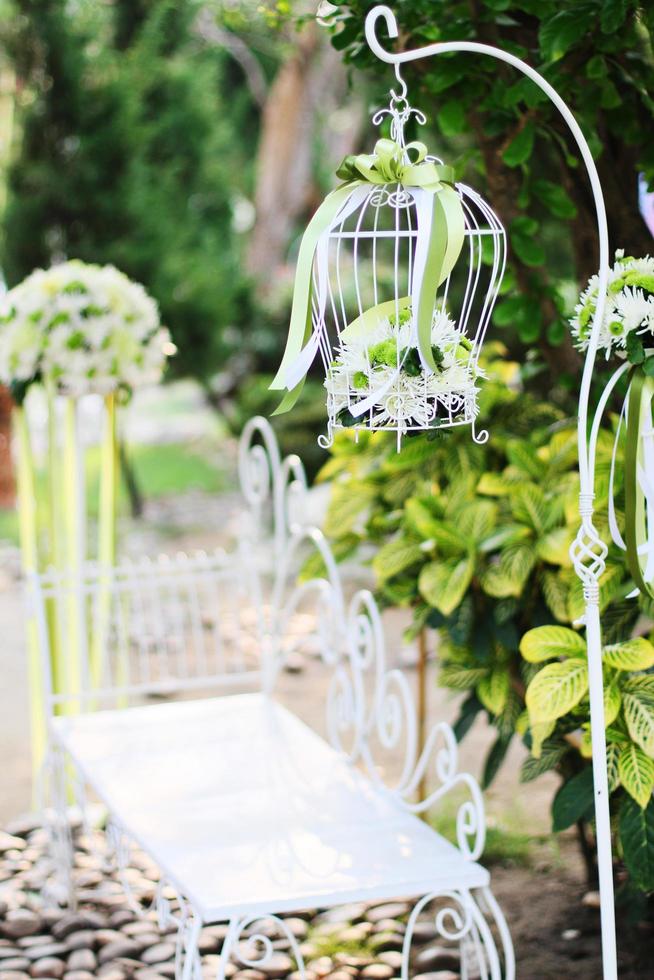 White birdcage, chair decoration with roses and white flowers hanging decoration in garden for wedding ceremony photo