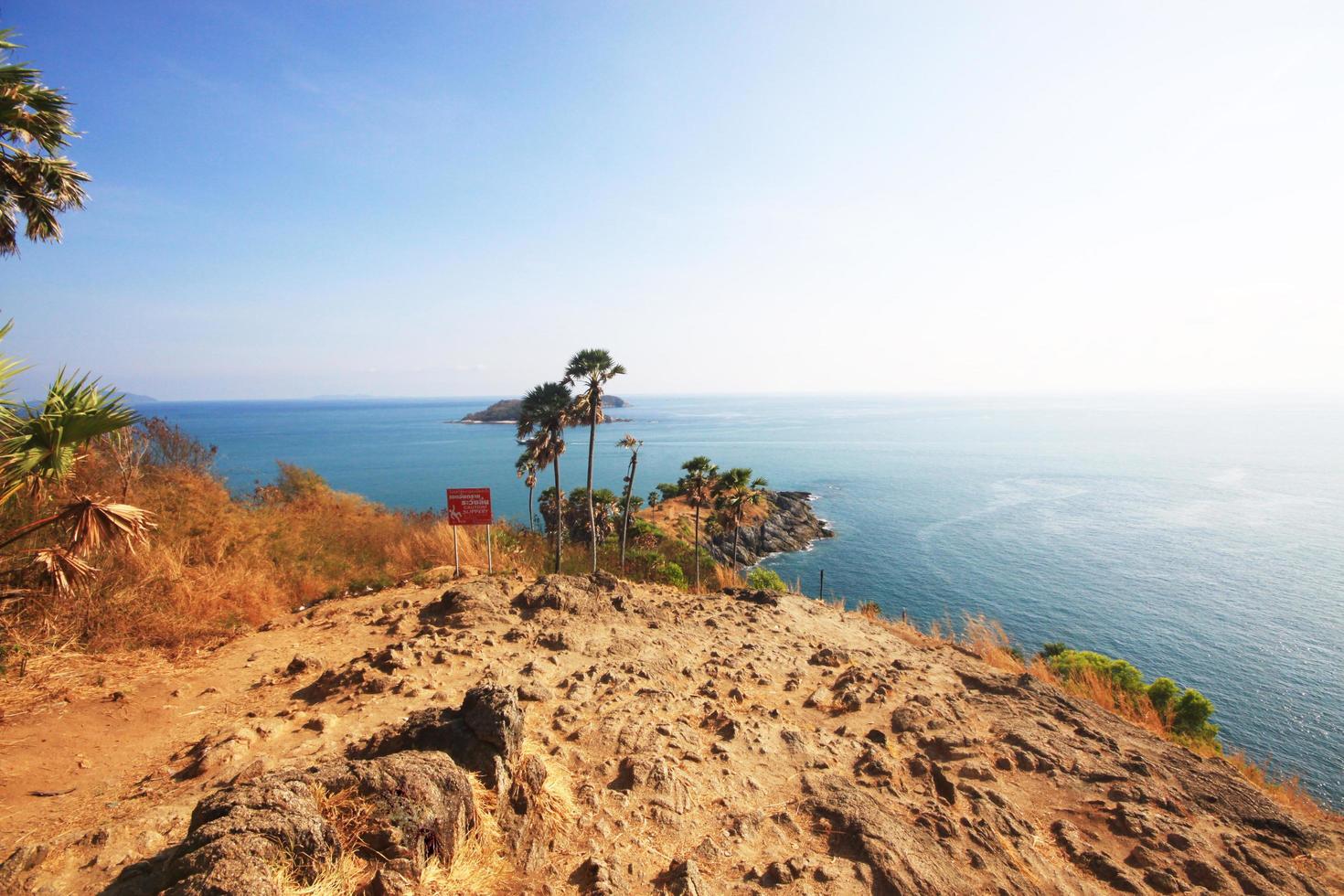 Caution slippery warning sign on rock mountain cape.Beautiful seascape with sunset and Palm tree on Dry grass field on mountain of Phrom Thep Cape in Phuket island, Thailand. photo