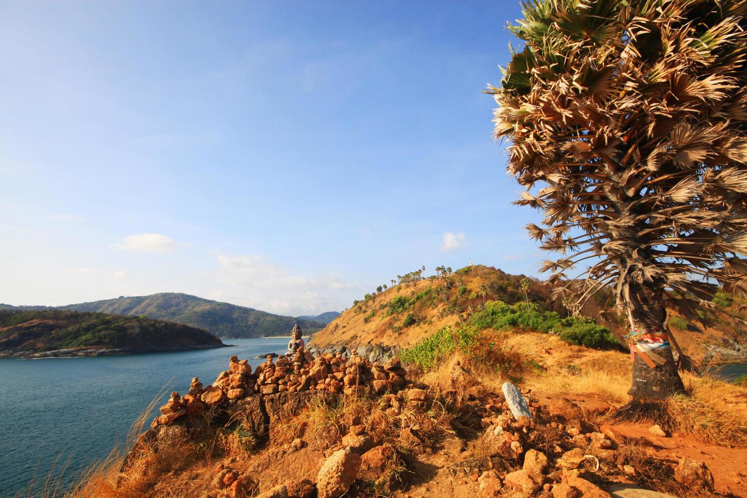 Beautiful Pyramid shape of stones arranged with Buddha statue in zen on rock mountain in seascape of sunset and sea horizon with Dry grass field on Phrom Thep Cape in Phuket island, Thailand. photo