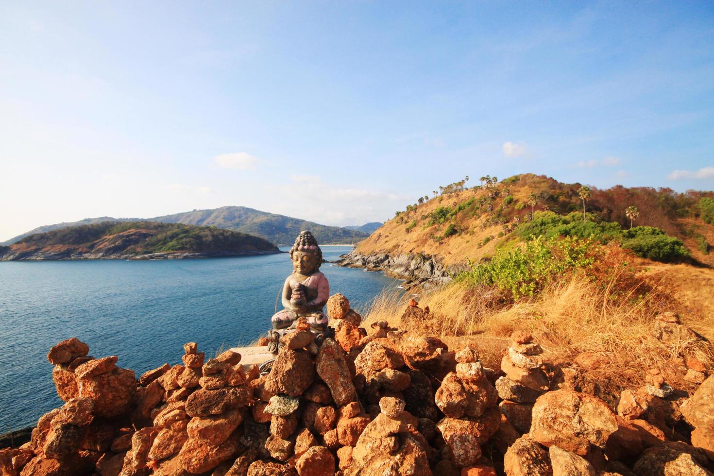 Beautiful Pyramid shape of stones arranged with Buddha statue in zen on rock mountain in seascape of sunset and sea horizon with Dry grass field on Phrom Thep Cape in Phuket island, Thailand. photo