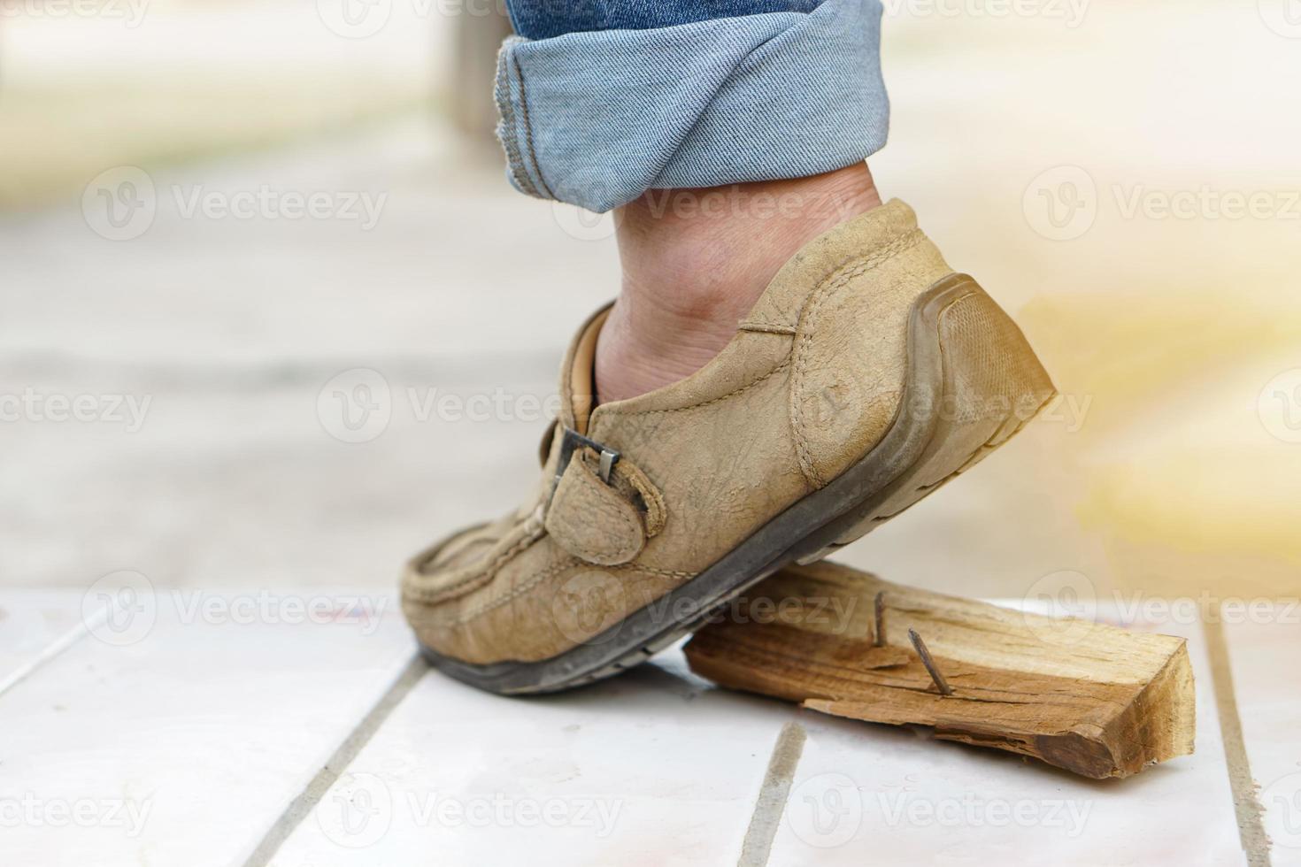 Closeup man wears shoes is stepping on rusty metal nail on wood. Concept, unsafe , risk for dangerous tetanus. Be careful and look around during walking at construction site or risk places. photo