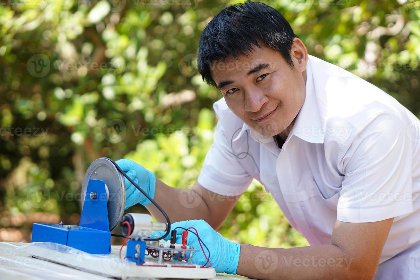 Asian man wears blue gloves demonstrate science experiment about electricity circuit from dynamo kit for teaching. Concept, science subject, project work. Experiment, education. Outdoor class. photo