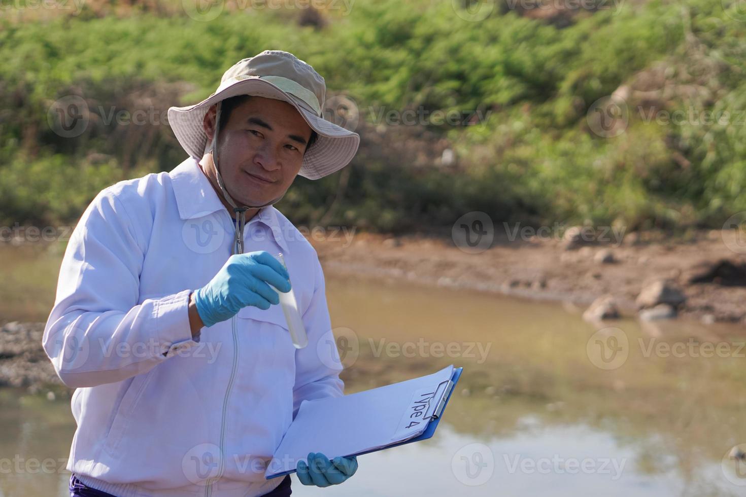 Asian man environment researcher holds tube of sample water to inspect from the lake. Concept, explore, analysis water quality from natural source. Ecology field research. photo