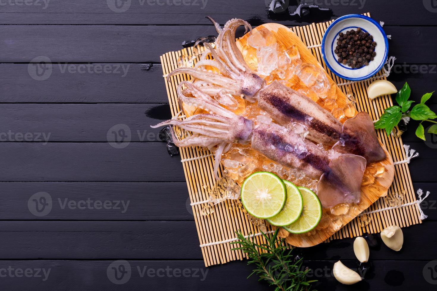 Raw squid on ice with lemon garlic spice salad on black wooden table background, fresh squid for cooked food at a kitchen restaurant or seafood market photo