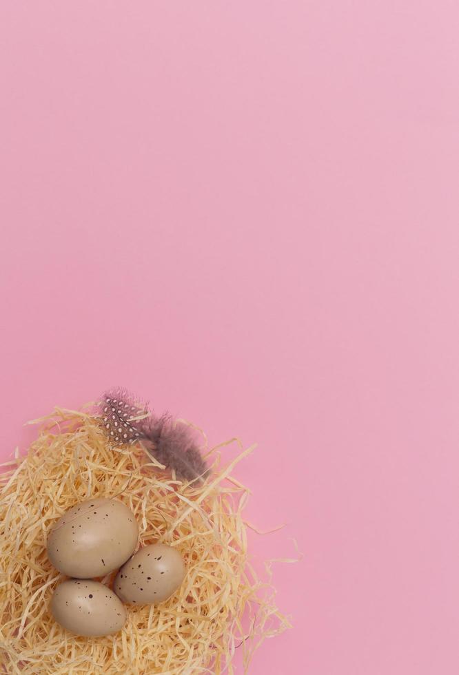 Easter eggs and feather in a nest on pastel pink Background. Minimal creative layout with copy space. Top view. Flat lay. photo