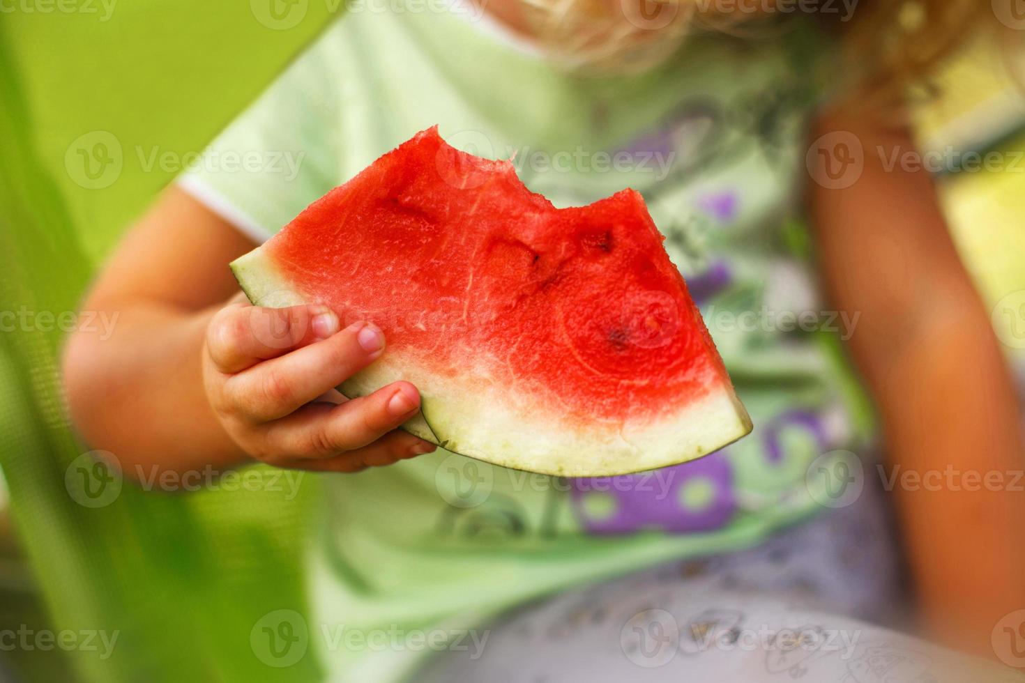 cute little girl holding a piece of watermelon close in the garden in summertime photo