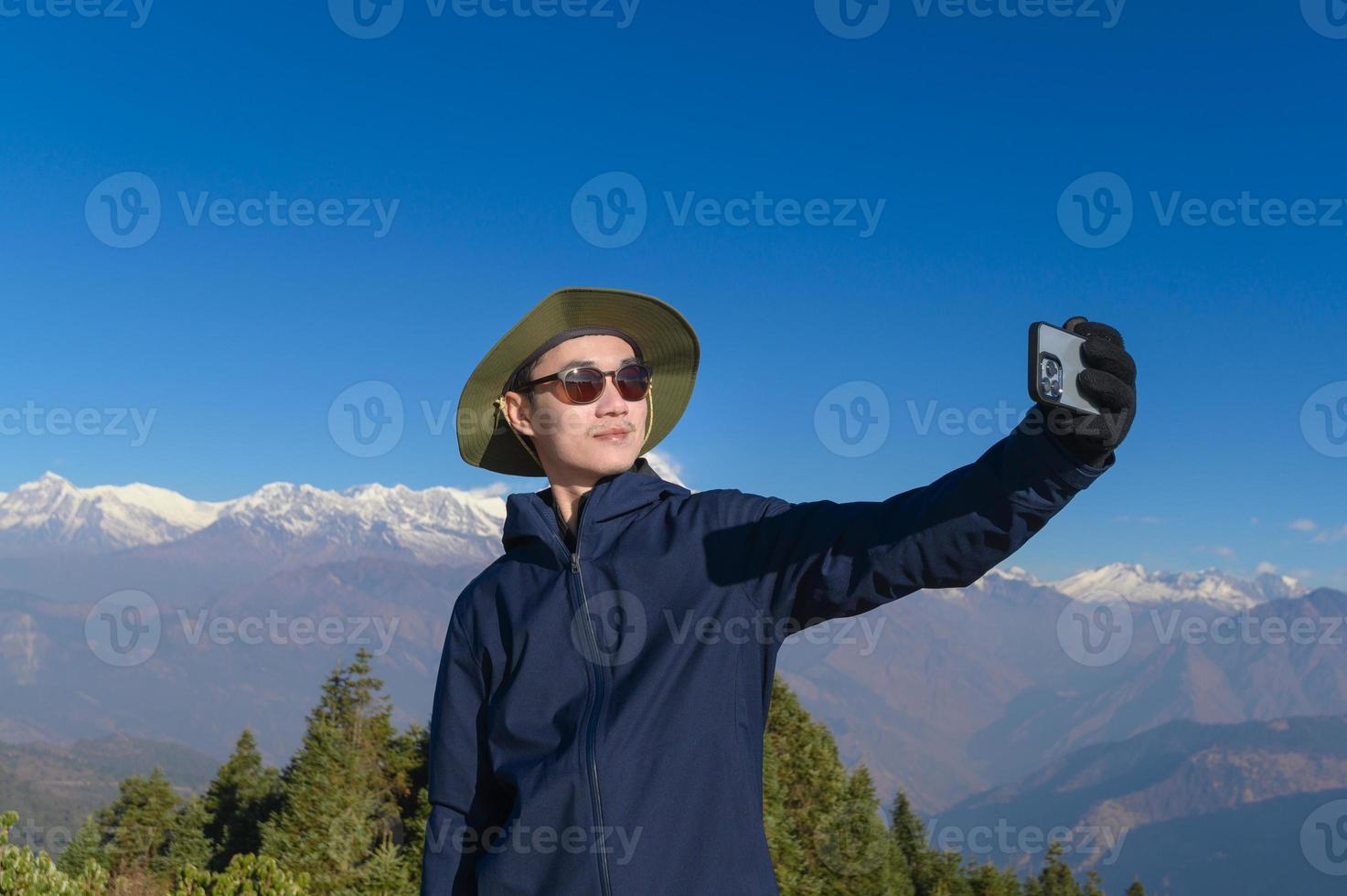 A young traveler takes a selfie or a video call while standing a top a mountain. photo