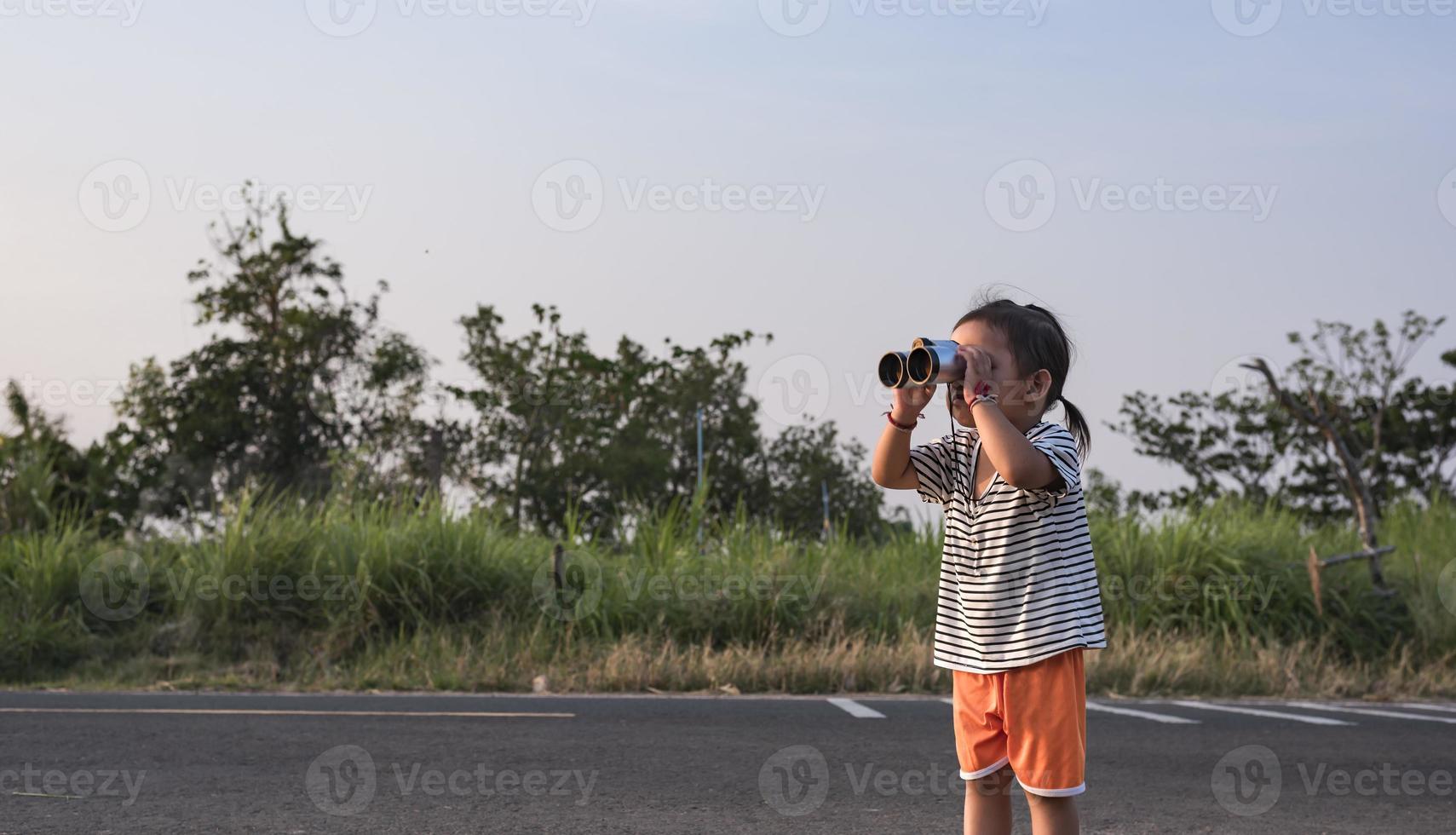 linda niña mirando mediante prismáticos, concepto de senderismo, cámping y aventura. foto