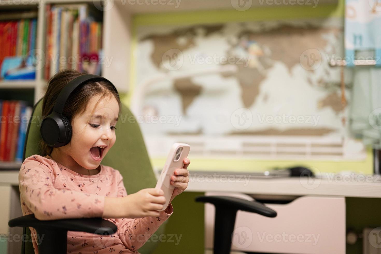 Little girl wear headphones watching cartoons or kid video on her phone. photo
