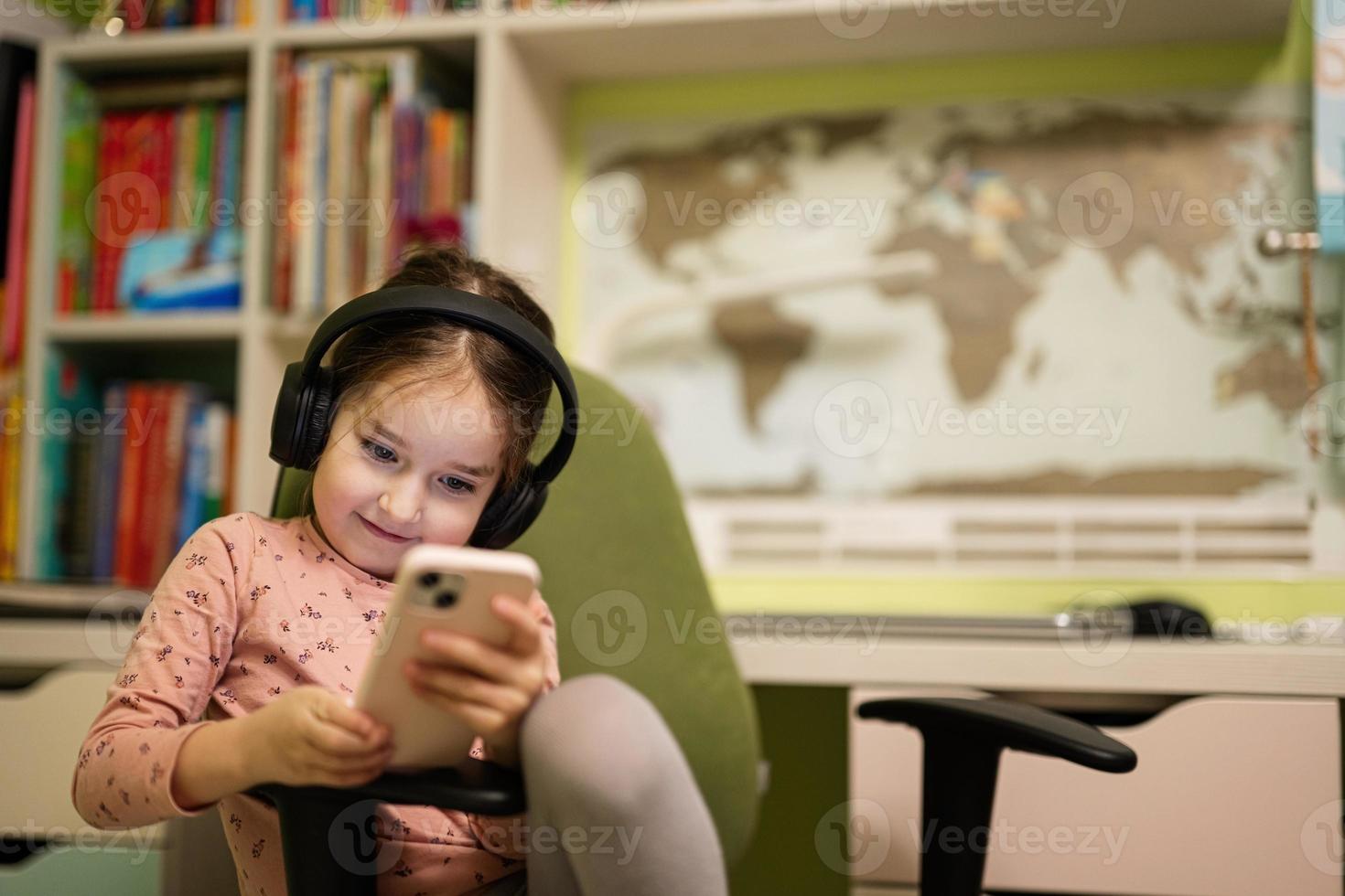 Little girl wear headphones watching cartoons or kid video on her phone. photo