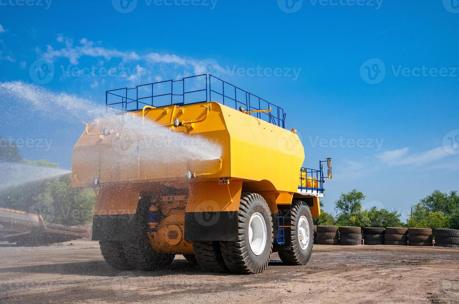 heavy yellow irrigating machine watering industrial area at sunny cloudless day photo