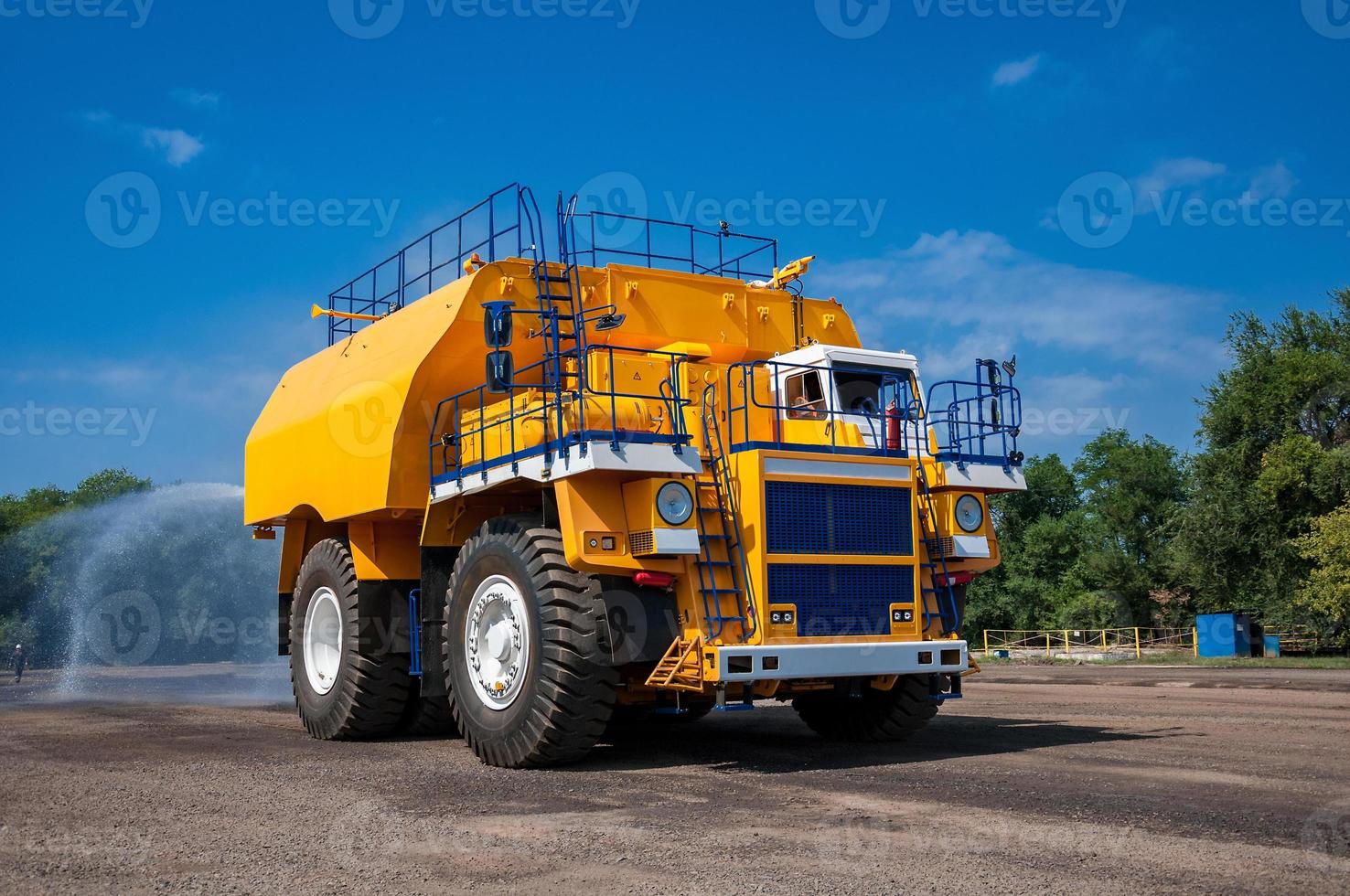 heavy yellow irrigating machine watering industrial area at sunny cloudless day photo