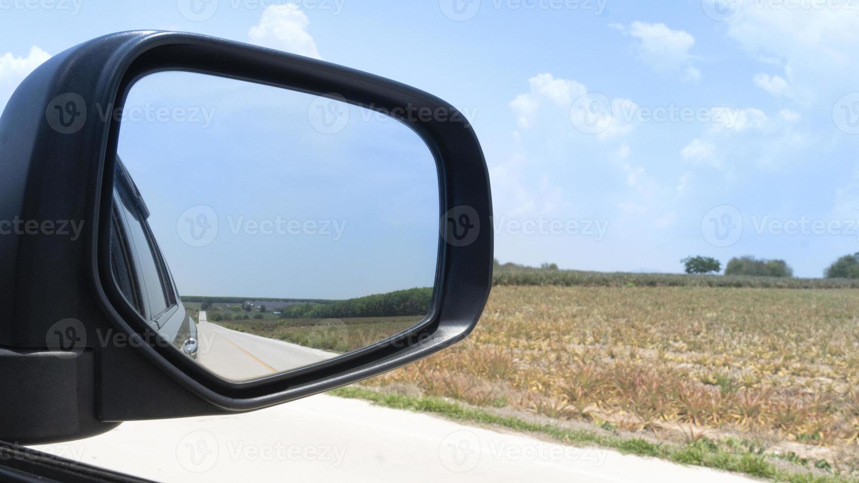 Car on the concrete road drive to nature. Travel to clear the province. Beside road with agricultural area of the seedlings of pineapple plantation under blue sky. Focus to mirror view backside. photo