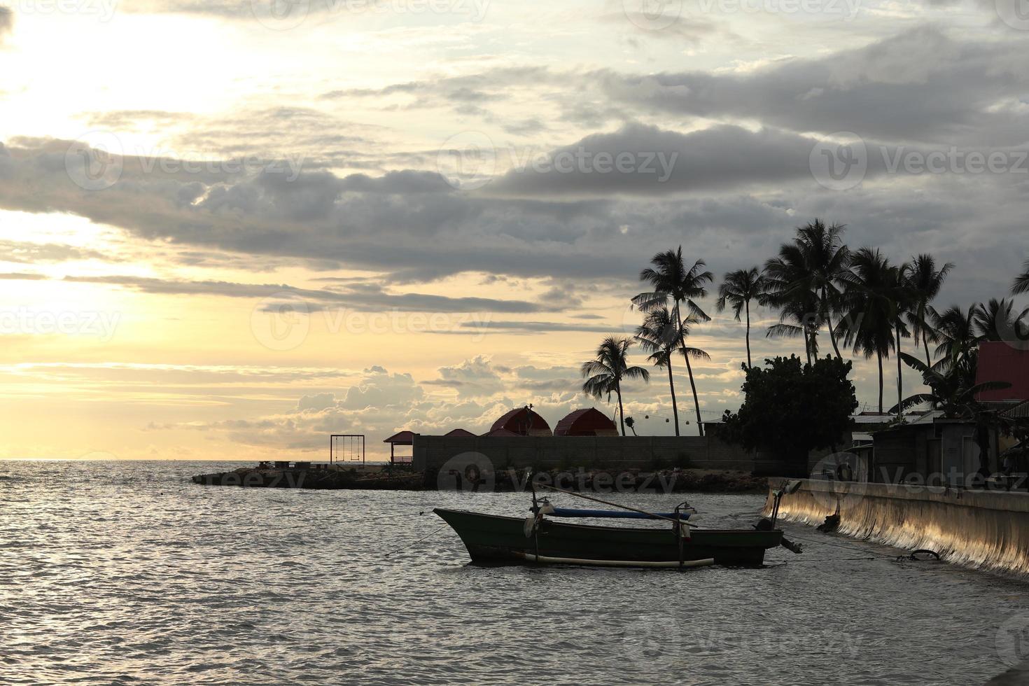 Silhouette of a fisherman's boat and a coconut tree on the beach with a sunset background photo