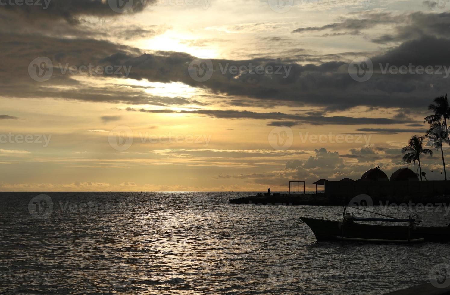 Silhouette of a fisherman's boat and a coconut tree on the beach with a sunset background photo