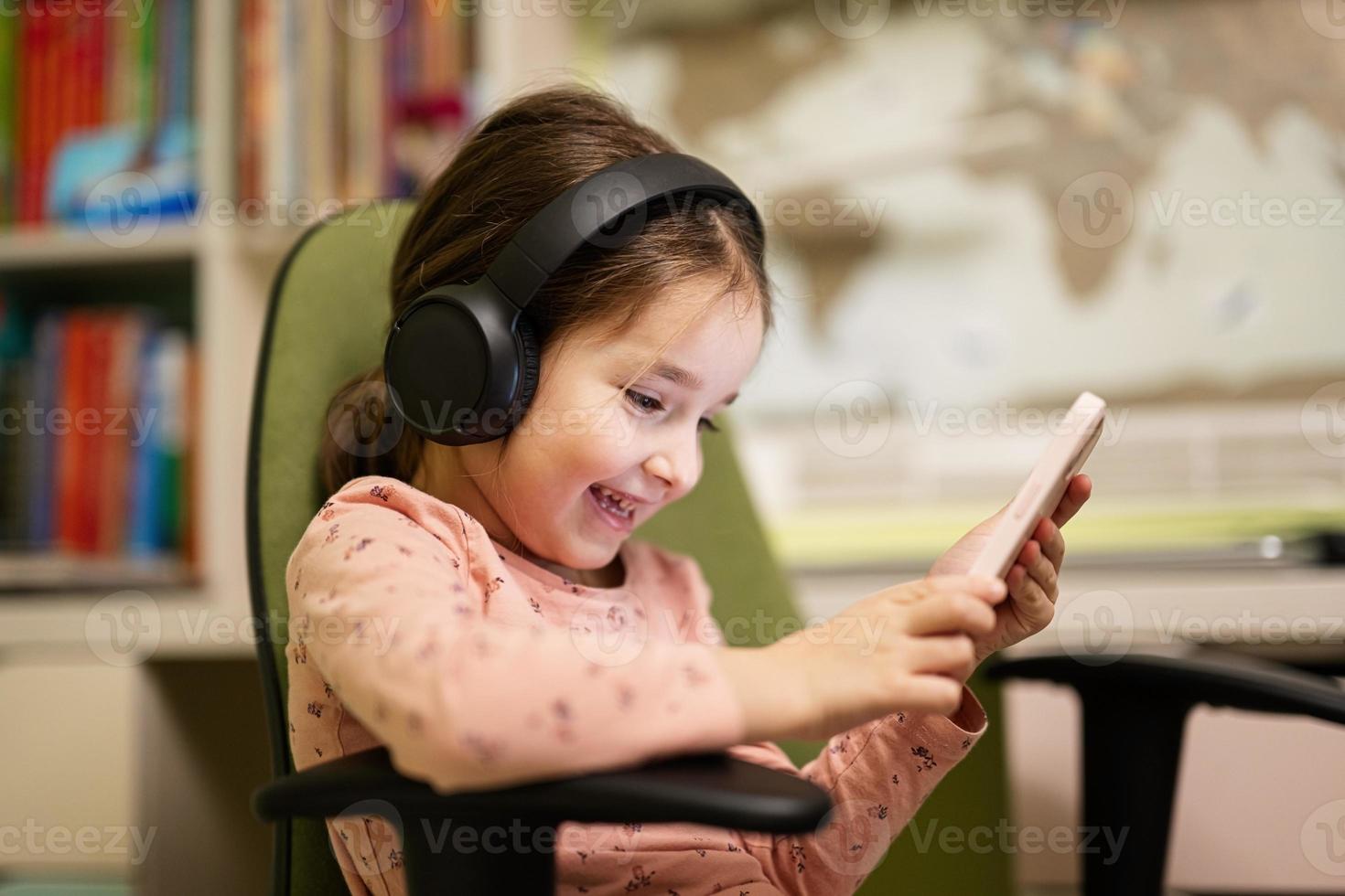 Little girl wear headphones watching cartoons or kid video on her phone. photo