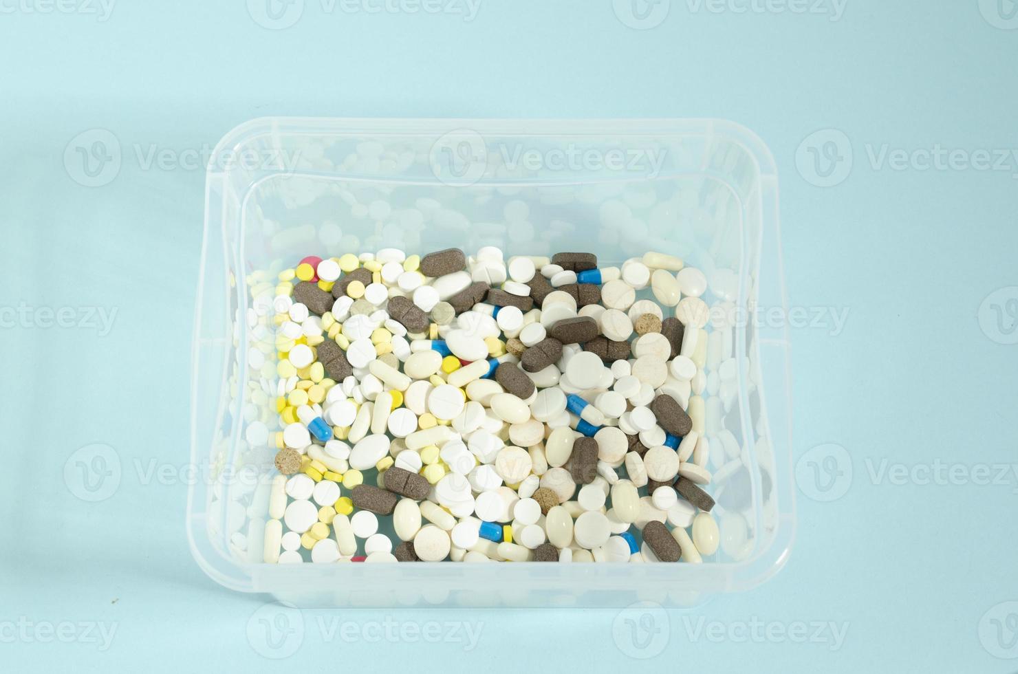 envase con pastillas multicolor y blanco pastillas en un transparente caja. pastillas en un azul antecedentes. foto