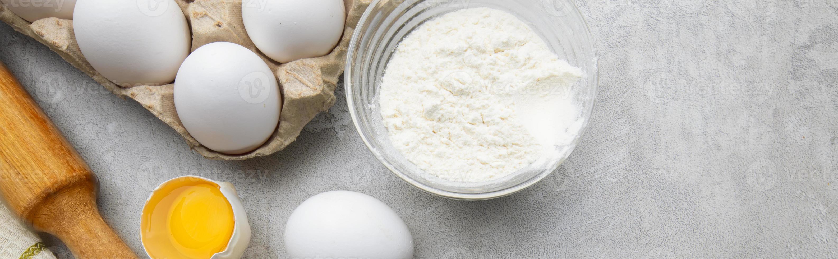 Baking cooking ingredients flour eggs rolling pin and kitchen textiles on gray concrete background. Cookie pie or cake recipe mockup photo