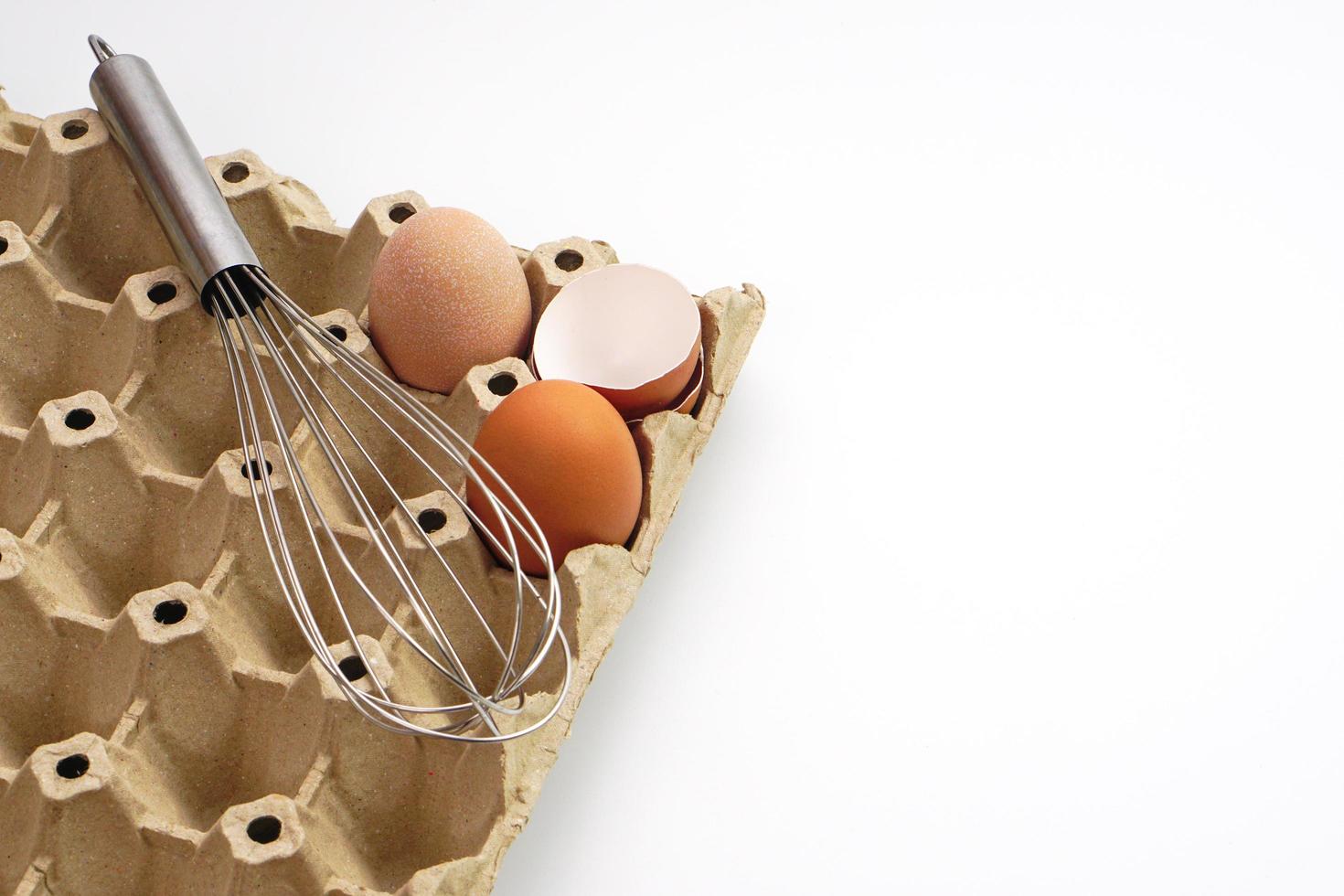 Chicken raw eggs in paper egg panel or in an egg stall and egg whisk on white background. Materials or kitchen equipment for bakery. photo