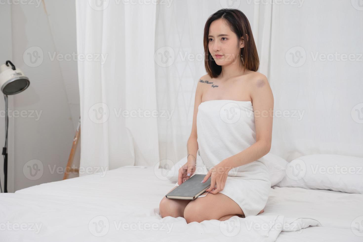 Portrait of white Asian woman with tattoo sitting on bed resting and relaxing inside white bedroom on her vacation holiday morning concept. photo