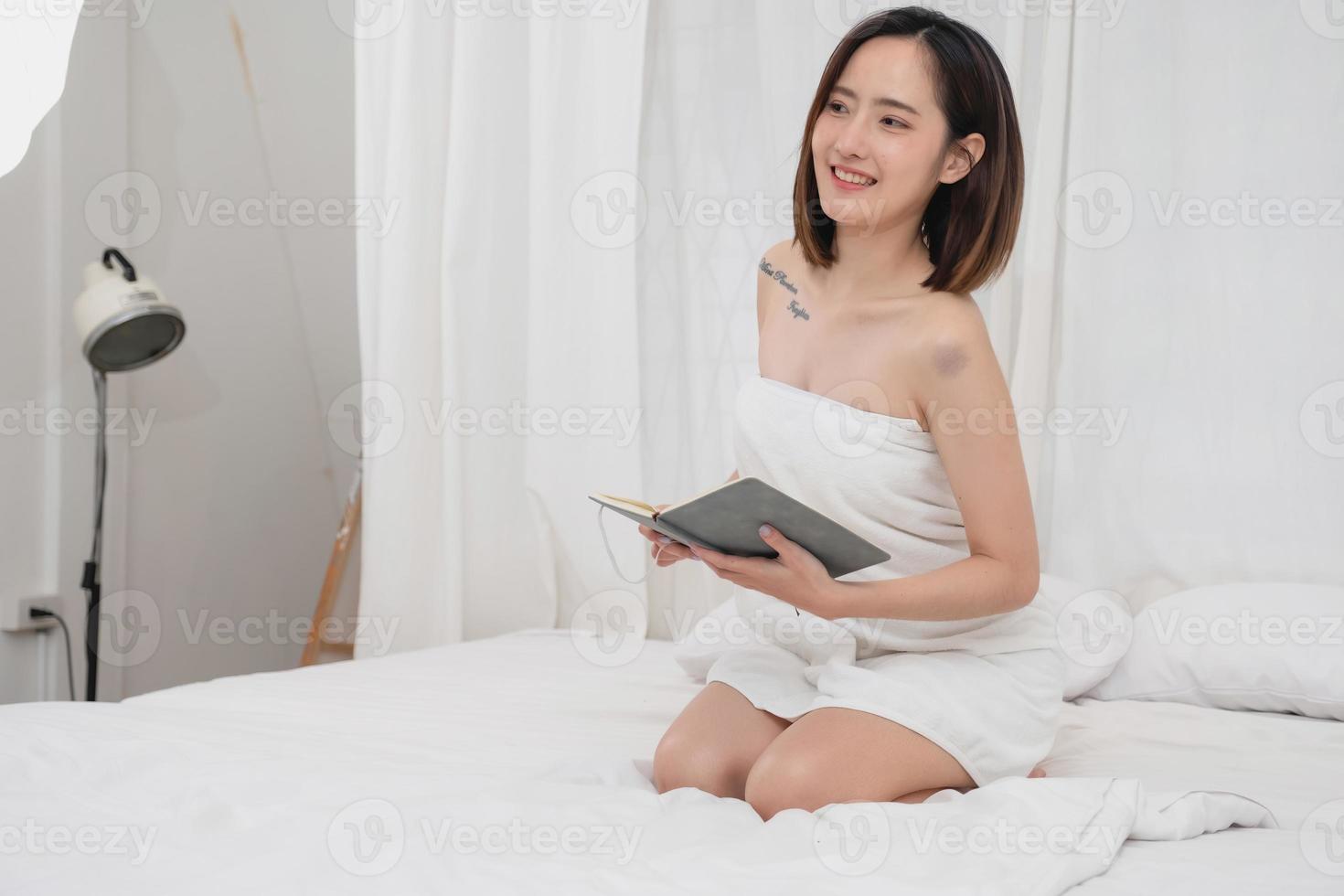 Portrait of white Asian woman with tattoo sitting on bed resting and relaxing inside white bedroom on her vacation holiday morning concept. photo